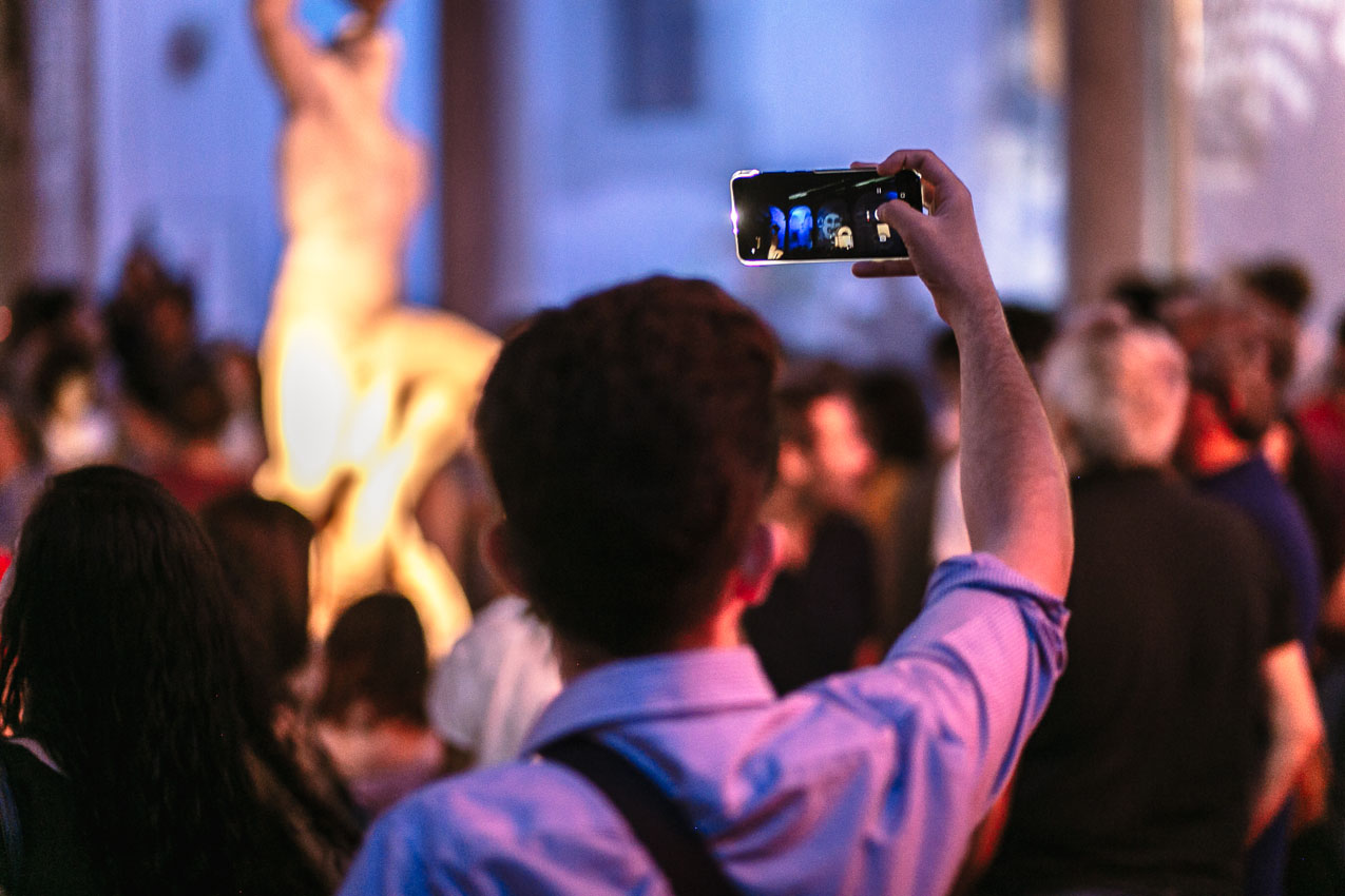 uomo che scatta una foto col cellulare agli ologrammi sul chiostro del museo salinas per inlumina