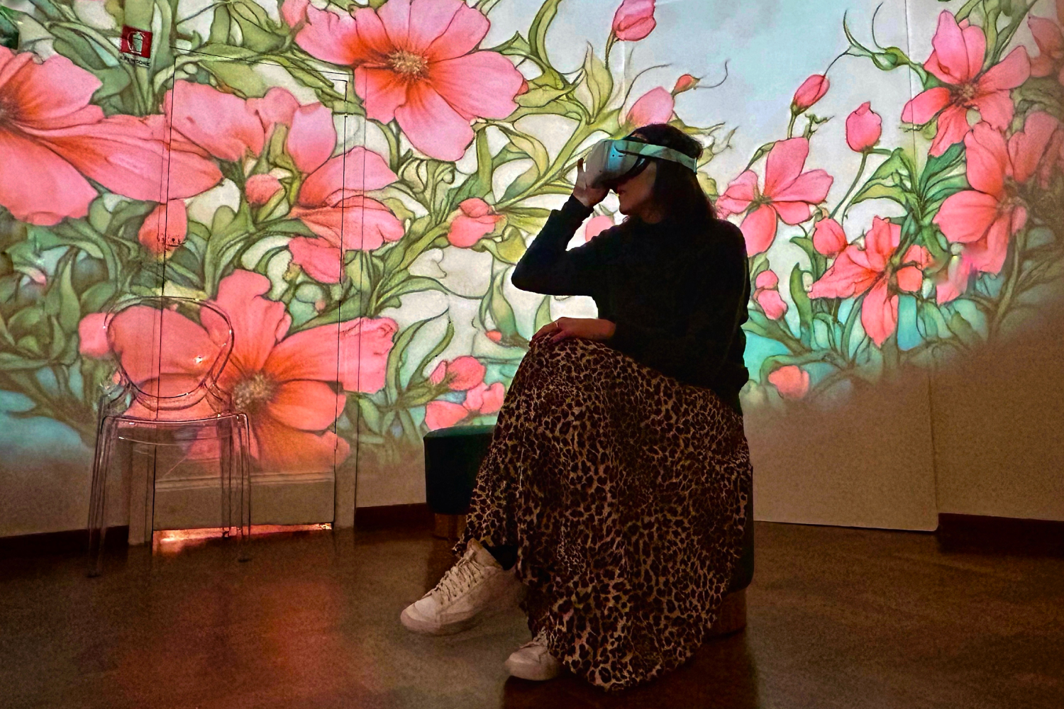 Donna seduta al centro della stanza con il visore di realtà virtuale indosso. Si trova all'interno della stanza immersiva della mostra Palermo Felicissima e sulle pareti sono proiettati a 360° dei fiori Art Nouveau
